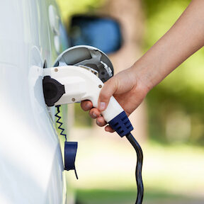 Extended hand inserting EV charger into side charging compartment of a vehicle 